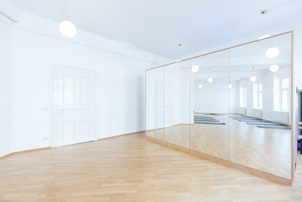Heller Yoga- und Tanzraum im Shoonya Studio in Graz mit großen Fenstern, Holzboden und Spiegelwand.